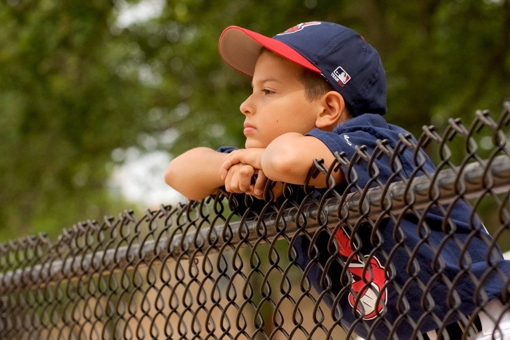 Young boy in his baseball uniform looking sad as he watches the game.